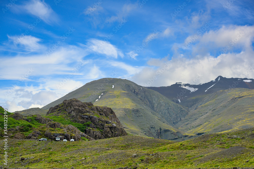 Many cars parked on the slopes. The background is high mountains with green grass all over the area. In the summer and blue sky days at countryside in Iceland Concept for traveling on holidays