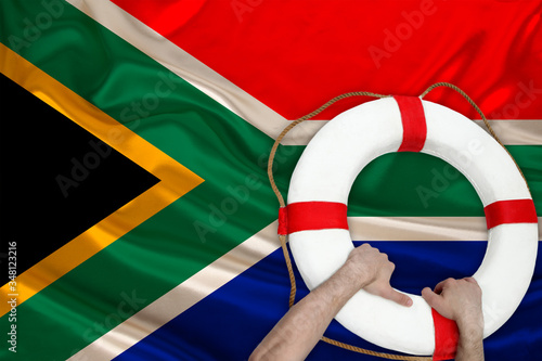 male hands hold on a white life buoy against the backdrop of the silk national flag of the country of South Africa, the concept of medical insurance, tourism, disaster, humanitarian aid
