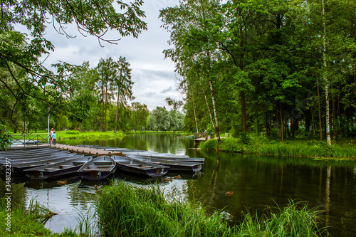 Summer landscape. A lake in the middle of a park. There is a pier and boats on the lake. Trees around the lake.