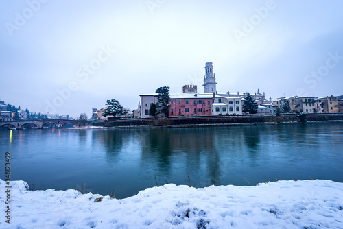 Fototapeta Naklejka Na Ścianę i Meble -  River Adige and Verona cityscape with the Ponte Pietra (Stone bridge, 1st century B.C.) and the bell tower of the Cathedral in winter with snow. Veneto, Italy, Europe