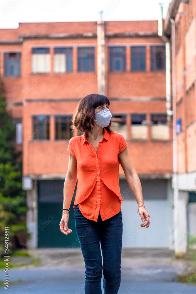 A young woman in a mask and orange shirt walking through the industry. Health emergency, pandemic Covid-19