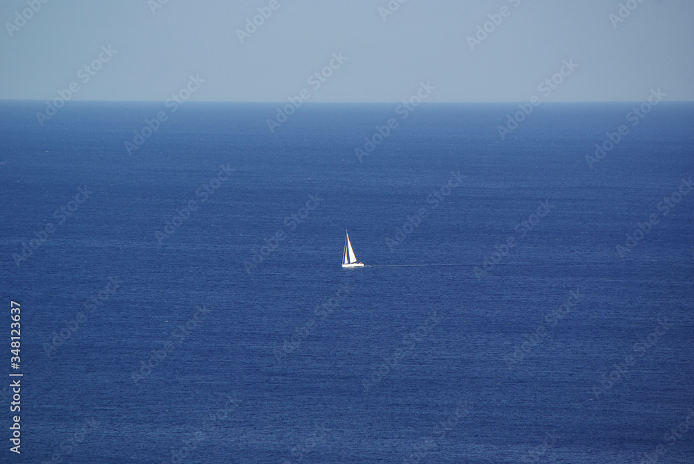 White sailboat in the distance on the blue sea