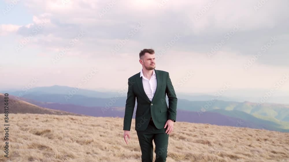 Portrait of a confident young brutal man walking on top of a mountain, businessman or politician on top of his career. against the backdrop of nature landscapes, amazing mountains. groom in a suit Portrait of a confident young brutal man walking on top of a mountain, businessman or politician on top of his career. against the backdrop of nature landscapes, amazing mountains. groom in a suit