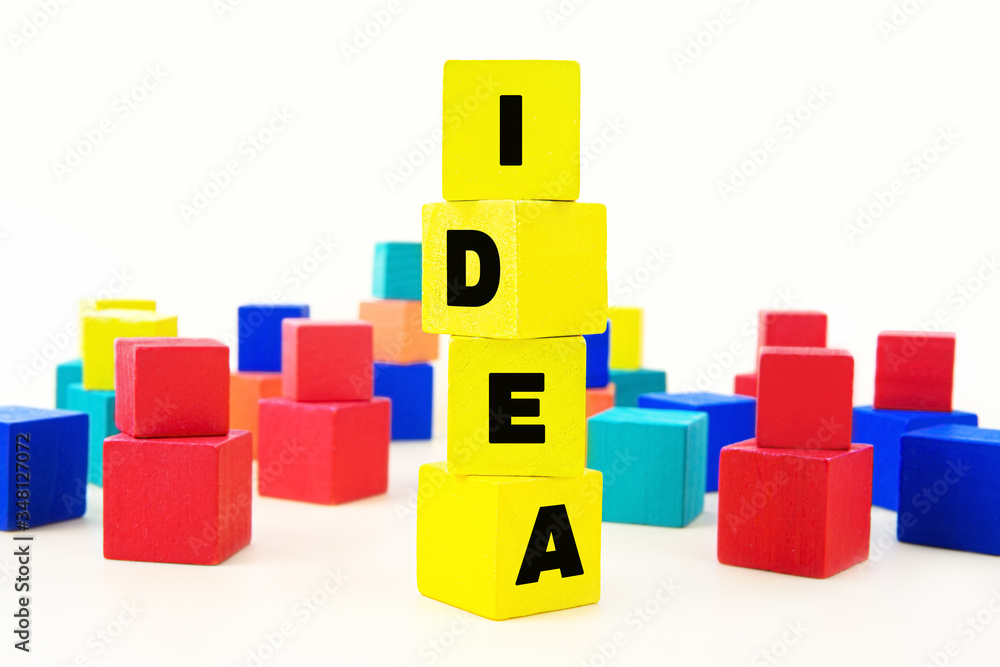 Word IDEA stacked of yellow wooden cube blocks and a lot of multicolored toy bricks in the background. White background, selective focus. Idea building, structuring and developing concept. Word IDEA stacked of yellow wooden cube blocks and a lot of multicolored toy bricks in the background. White background, selective focus. Idea building, structuring and developing concept.