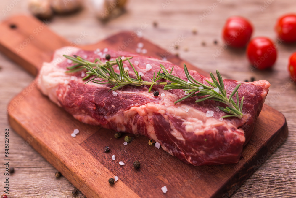 Raw meat. A large piece of beef chop on a wooden cutting board with rosemary and spices, close-up.