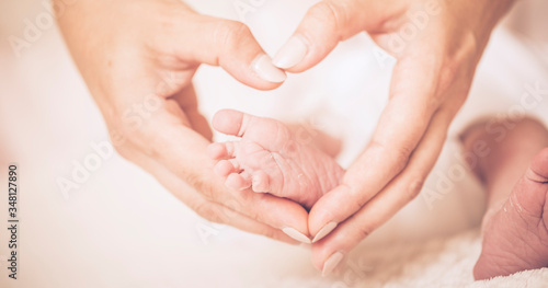 Newborn baby feet on mom and dad hands, shape like a lovely heart.