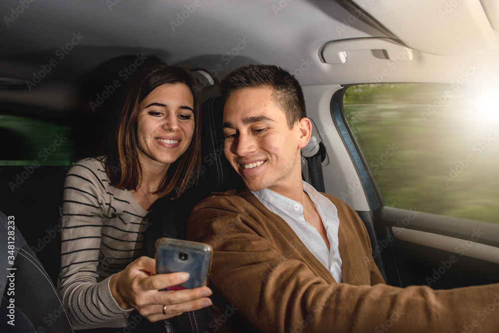 Caucasian couple inside car. Man driving and woman holding smartphone to write emails, select music or app navigation maps showing something to the boy. moving car.