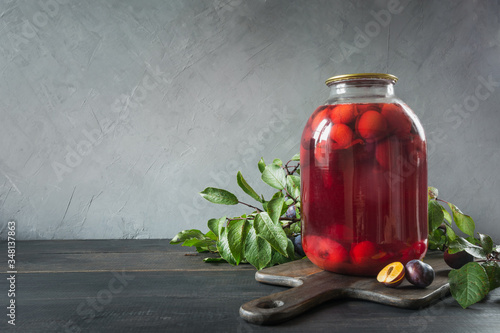 Photos Homemade canned plum compote in large glass jar on wooden board