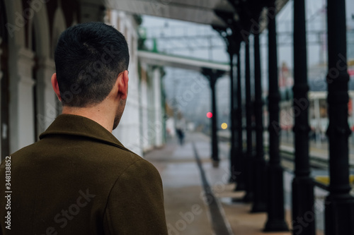 A young man is standing on the railway station with his back to the camera 