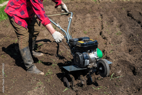 Old man plows the ground with a motor cultivator. A farmer ploughs the soil using a petrol cultivator.