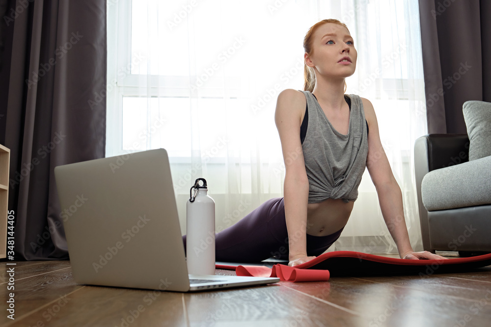 The girl is engaged in stretching at home in front of a laptop. Exercise on stretching the lower back and back The girl is engaged in stretching at home in front of a laptop. Exercise on stretching the lower back and back
