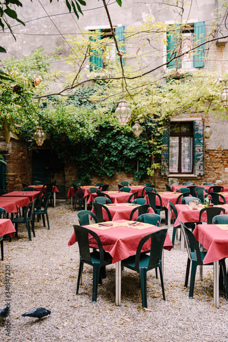 Fototapeta Naklejka Na Ścianę i Meble -  Empty cafe because of the coronavirus COVID-19 pandemic. Empty cafe in the patio on the street in Venice, Italy. Square tables with red tablecloth, green plastic chairs. 
