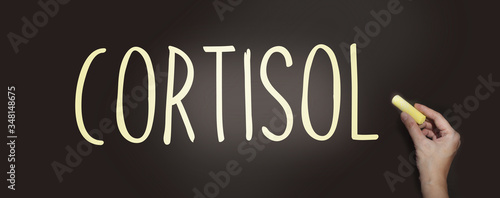 Cortisol word on a blackboard and hand with yellow chalk. Healthcare medical concept photo