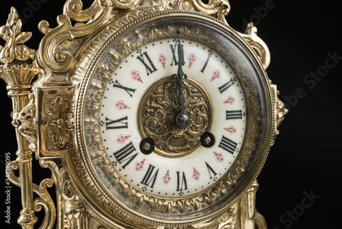 dial of vintage bronze clock on black background, antique clock photo close up, old bronze clock in gilding, twelve o'clock on the dial 