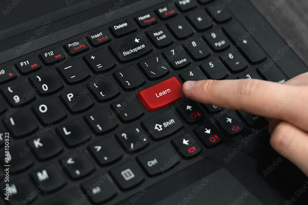 Index finger presses the red button on the black laptop keyboard. Computer keyboard with red key 'Learn' . Distance and e-learning education concept, online lessons Index finger presses the red button on the black laptop keyboard. Computer keyboard with red key 'Learn' . Distance and e-learning education concept, online lessons