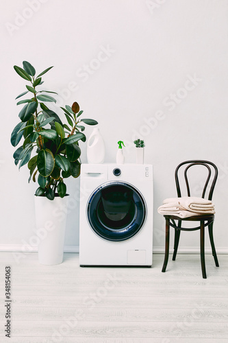 modern bathroom with plants, detergent and spray bottles, towels and chair near washing machine