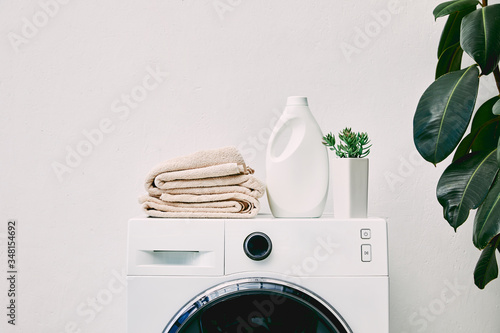 Detergent bottle and towels on washing machine and green plant in bathroom Fototapet