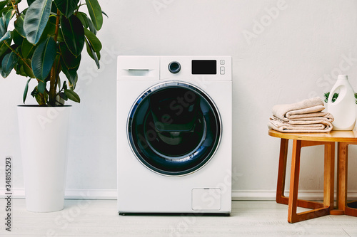 Photos green plant near washing machine, wooden coffee table with towels and detergent