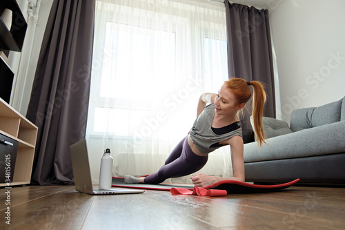 The red-haired girl stands on the mat of the house in the side bar and looks into the laptop, frame from below. 