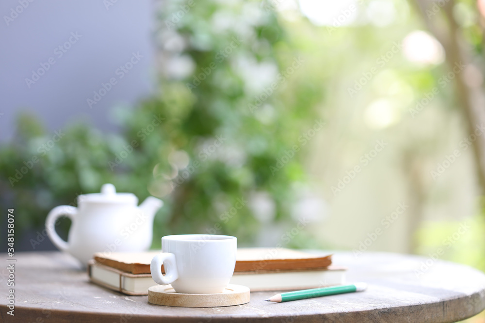 White tea kettle and white cup with notebook and pencil on wooden table outdoor view White tea kettle and white cup with notebook and pencil on wooden table outdoor view