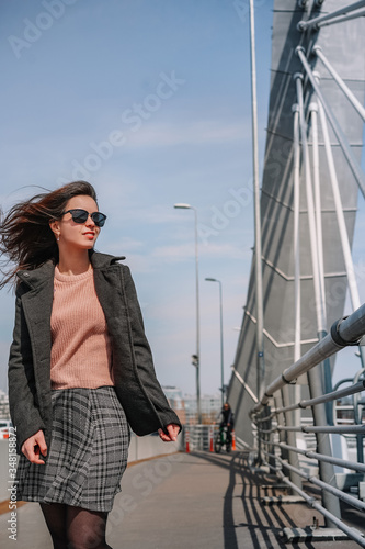 A young brunette girl in a coat and skirt stands on a bridge, beautiful metal structures in the air, hair flying in the wind, business issues, construction engineering © KseniaJoyg