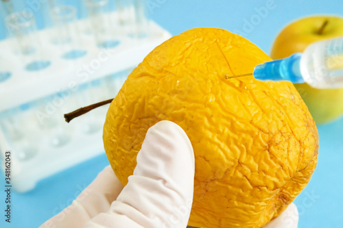 apple in genetic engineering laboratory with syringe and test tubes on blue background, gmo food concept