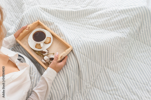  woman sits in bed in the bedroom and holds a tray with coffee and cookies at dawn. eating in bed on a white background in the morning with breakfast