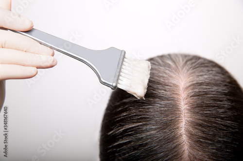 Woman dyeing grey hair root with brush and hair color, close up