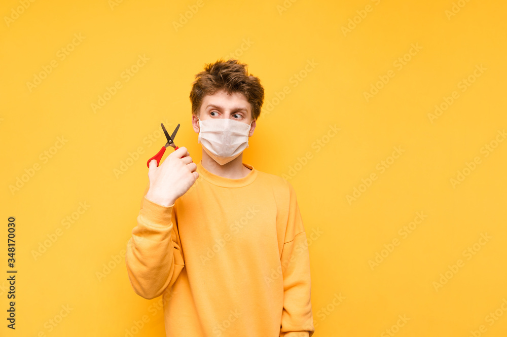 Portrait of a shaggy man in a medical mask on a yellow background, holding a scissors for a haircut and going to cut long hair on his head. Quarantined haircut. Portrait of a shaggy man in a medical mask on a yellow background, holding a scissors for a haircut and going to cut long hair on his head. Quarantined haircut.