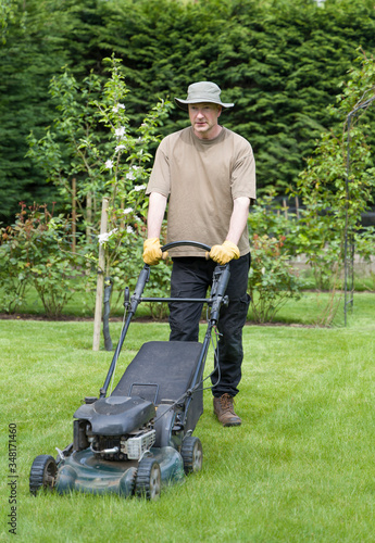 Man mowing lawn in a garden in summer, UK