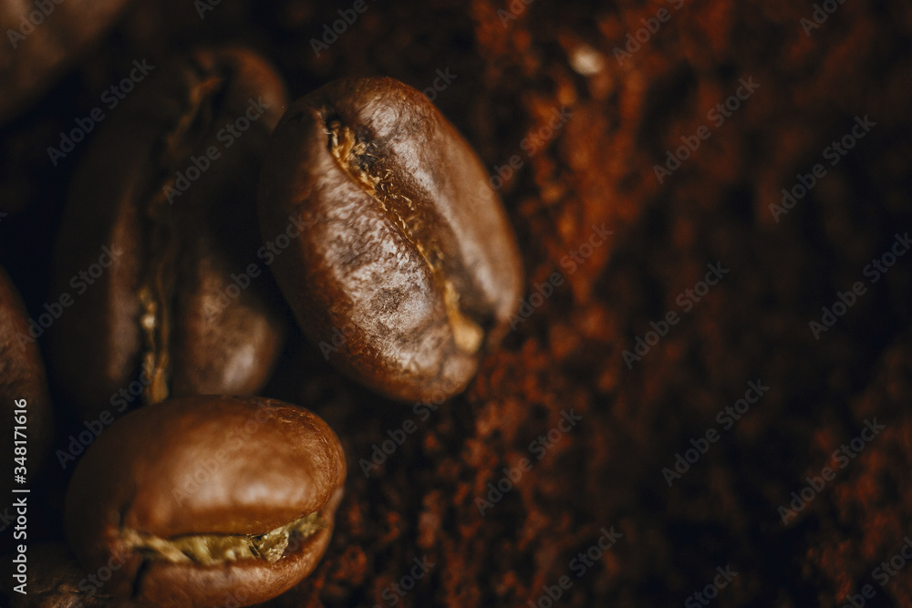 Fresh aromatic roasted coffee beans macro view. Coffee beans close up on grounded coffee pile. Space for text. Brown tone moody image Fresh aromatic roasted coffee beans macro view. Coffee beans close up on grounded coffee pile. Space for text. Brown tone moody image