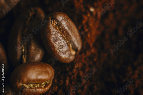  Fresh aromatic roasted coffee beans macro view. Coffee beans close up on grounded coffee pile. Space for text. Brown tone moody image