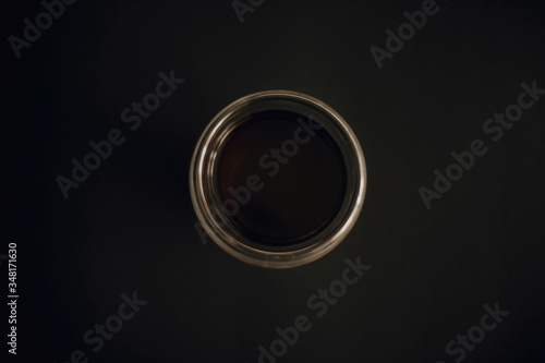 Fresh coffee in glass cup on black background flat lay with copy space. Minimalism. Drip or filter coffee. Dark moody image. Coffee brewing. Glass circle