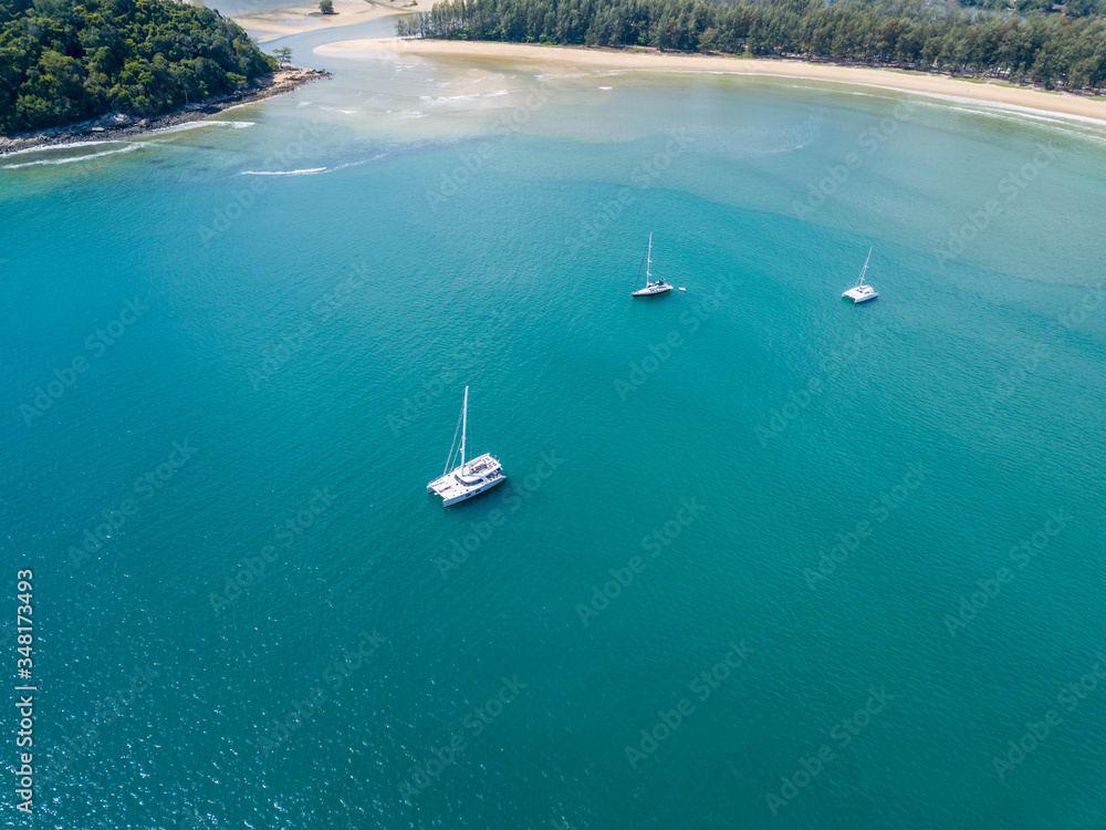 A view from a high-angle drone sees sailboats leaving the anchor in a beautiful bay.