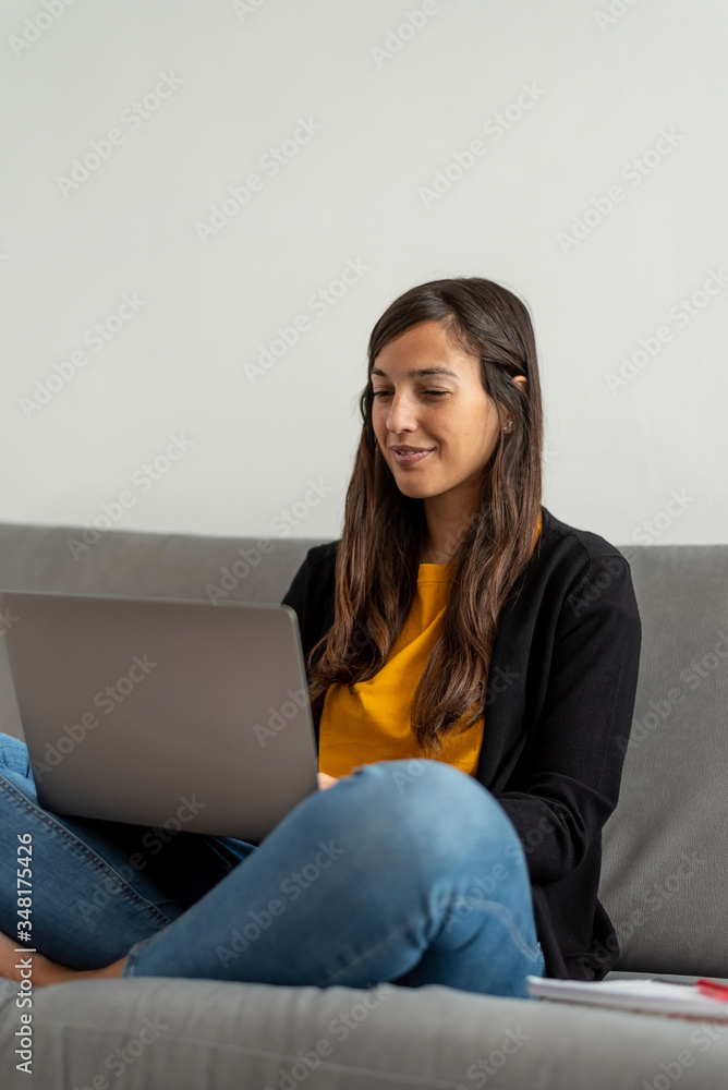 Young woman with laptop telecommuting on the sofa at her home Young woman with laptop telecommuting on the sofa at her home