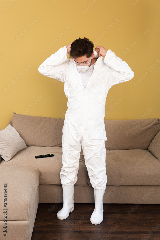 Man in medical mask and safety goggles wearing hazmat suit in living room Man in medical mask and safety goggles wearing hazmat suit in living room