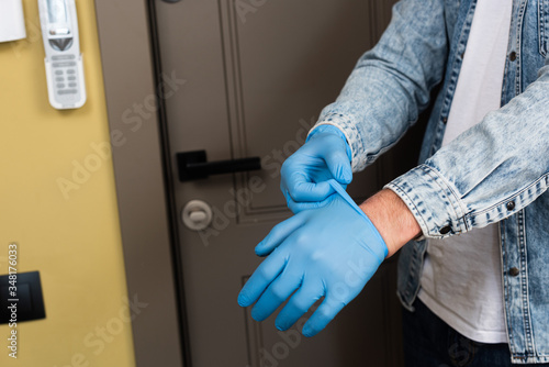 Cropped view of man putting on latex gloves near door at home