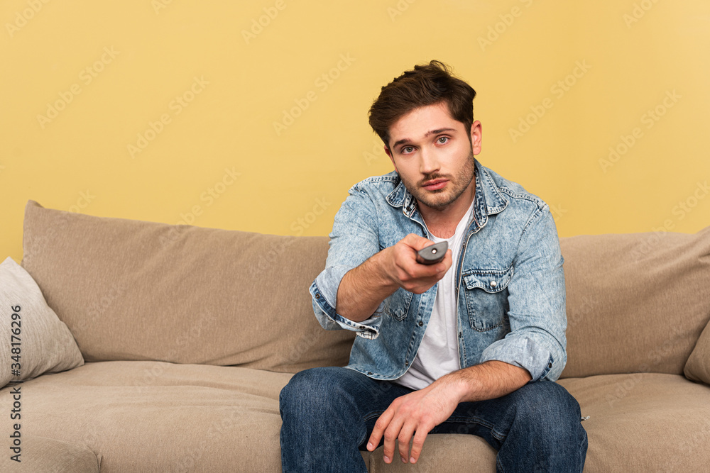 Handsome man holding remote controller while sitting on couch Handsome man holding remote controller while sitting on couch