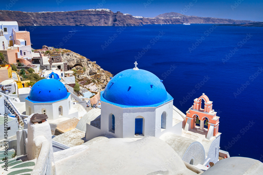 Blue church domes and white houses in the beautiful Oia town on the Santorini island, Greece.
