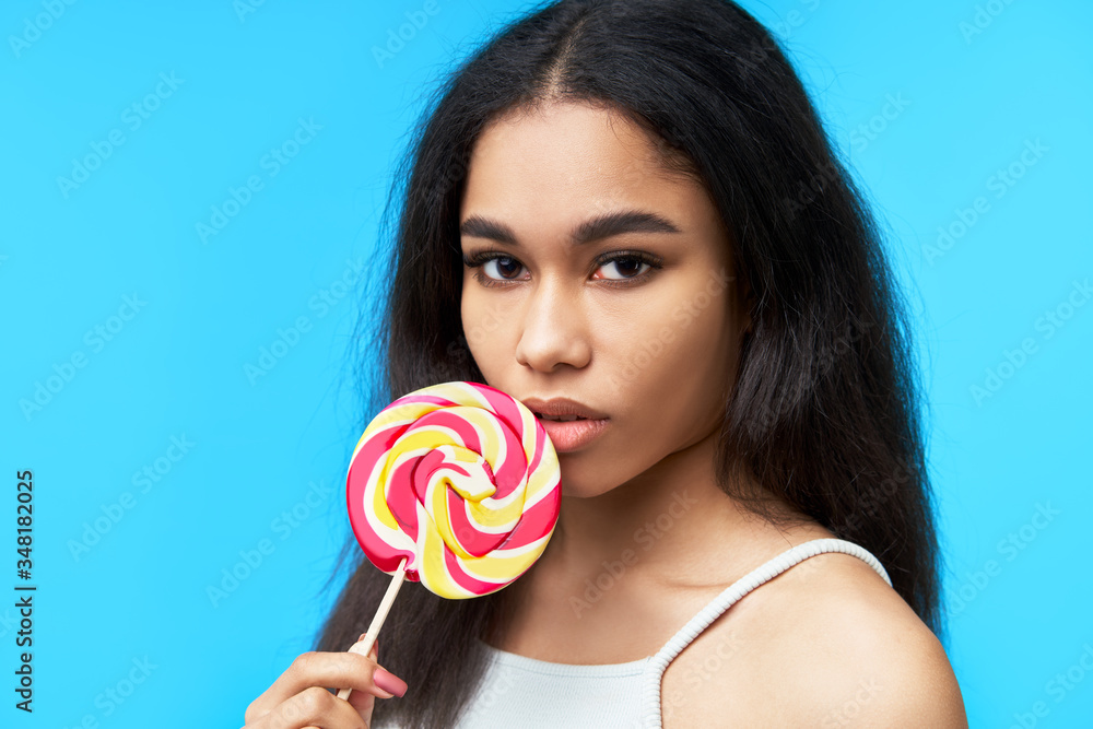 Pretty black woman with colorful lollipop on blue background