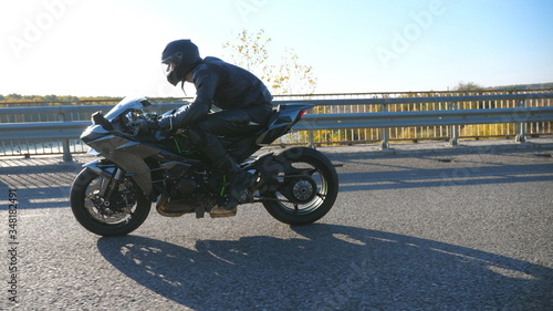 Young man in helmet riding fast on modern sport motorbike at highway. Motorcyclist racing his motorcycle on country road. Guy driving bike during trip. Concept of adventure. Side view Close up