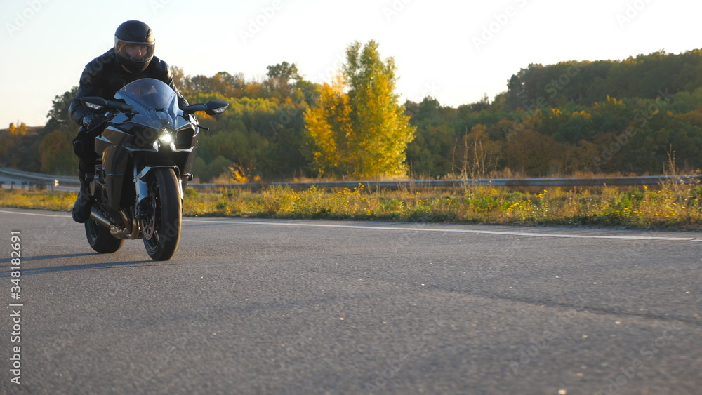 Motorcyclist racing his motorcycle on autumn country road. Young man in helmet riding fast on modern sport motorbike at highway. Guy driving bike during trip. Concept of freedom and adventure