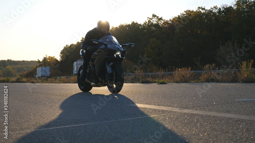 Man in helmet riding fast on modern sport motorbike at highway with sun flare at background. Motorcyclist racing his motorcycle on country road. Guy driving bike during trip. Concept of freedom © olehslepchenko