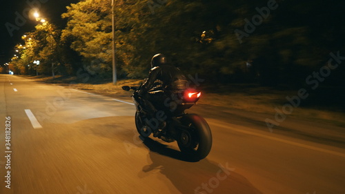 Motorcyclist racing his motorcycle on evening city. Man riding on modern sport motorbike at night street of town. Guy driving bike during trip. Concept of freedom and adventure. Rear view Close up