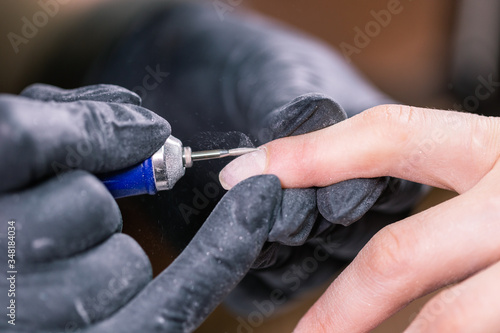 Manicurist use electric nail file drill in beauty salon. Perfect nails manicure process close up with burst flying debris.