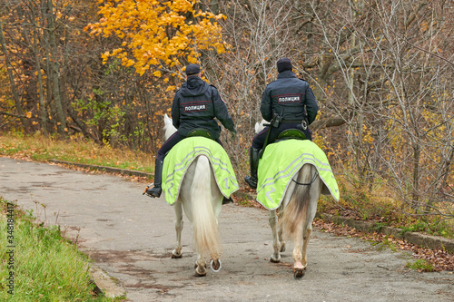 Mounted police in autumn city park, back view