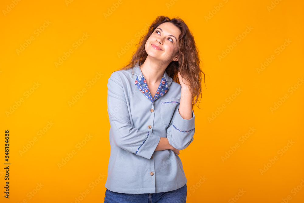 Excited young woman with curly hair in blue home wear, widely smiling having fun. Isolated on yellow background. Excited young woman with curly hair in blue home wear, widely smiling having fun. Isolated on yellow background.