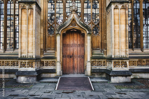 Exterior of the Divinity School in Oxford showing a big wooden door entrance and columns and stained glass windows photo