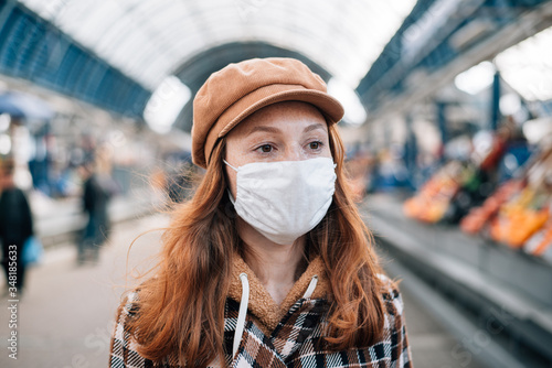 Red hair girl in a protective mask walks the market during the coronavirus epidemic. Girl in face mask is walking through rows with vegetables and fruits.