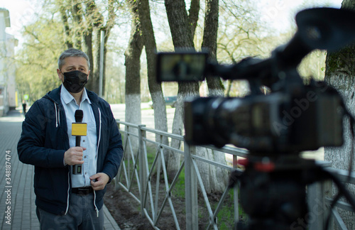 A middle- aged European journalist in a protective medical mask is reporting in a deserted city.